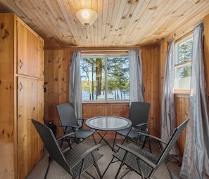 A cabin with wooden walls, a round table with four chairs, and a window with curtains.