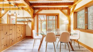 A dining area with a glass table and chairs, wooden beams, and large windows. - New! Acadia Nature Escape w/Trails + Water Access (Sullivan)