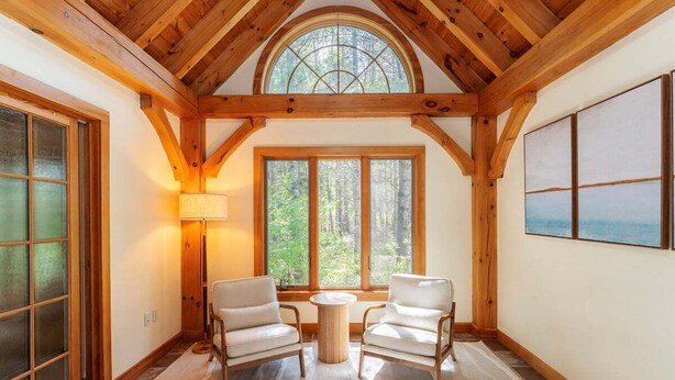A room with wooden beams, a large window, two chairs, a lamp, and a painting on the wall. - New! Acadia Nature Escape w/Trails + Water Access (Sullivan)