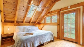 A bedroom with a wooden ceiling, a bed with a gray bedspread, a nightstand, and a window with a view of greenery. - New! Acadia Nature Escape w/Trails + Water Access (Sullivan)
