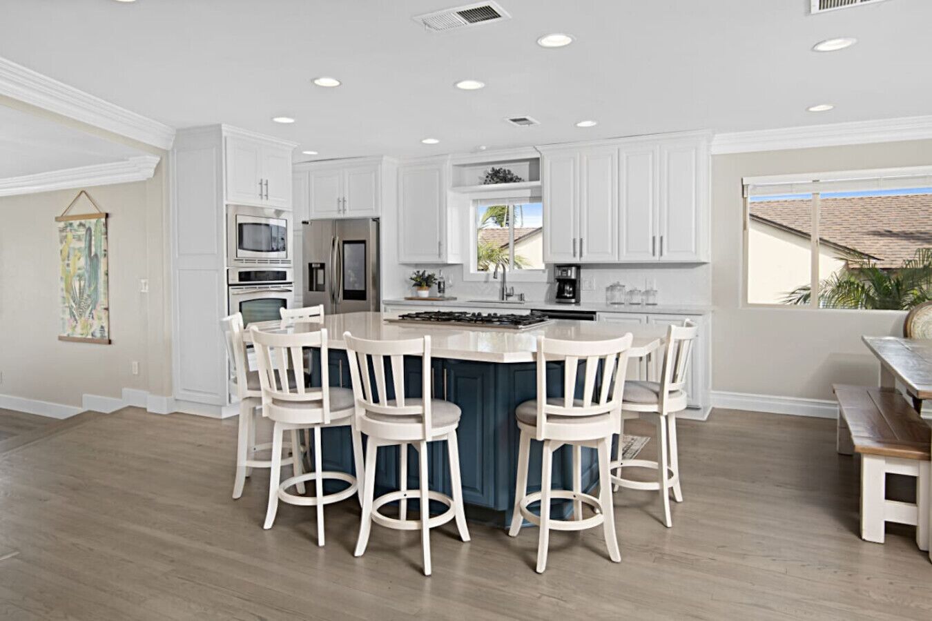 A modern kitchen with white cabinetry, a central island with bar stools, and a large window providing a view of the outside.