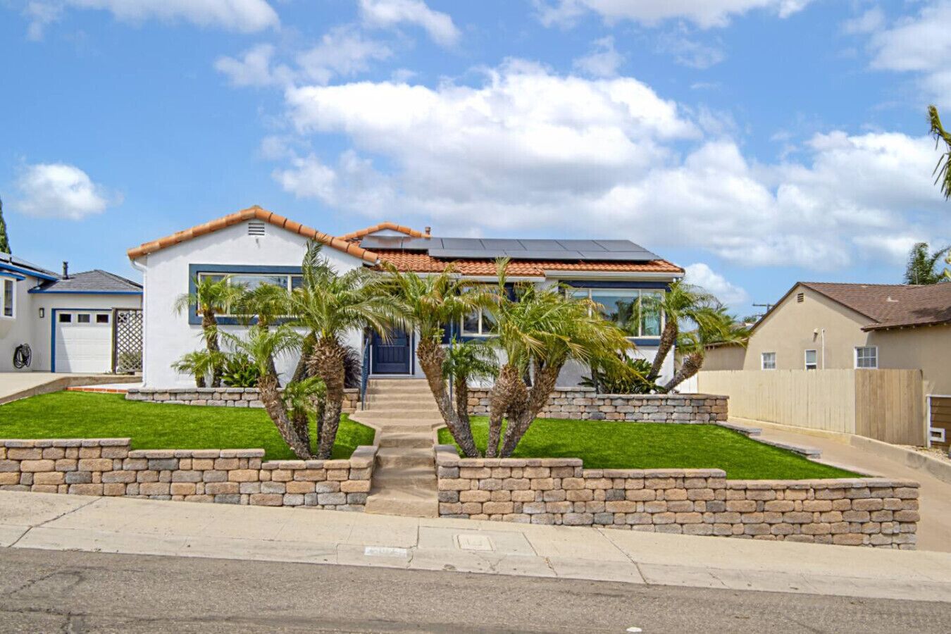 A modern two-story house with a front entrance, a garage, and a well-maintained lawn with palm trees.
