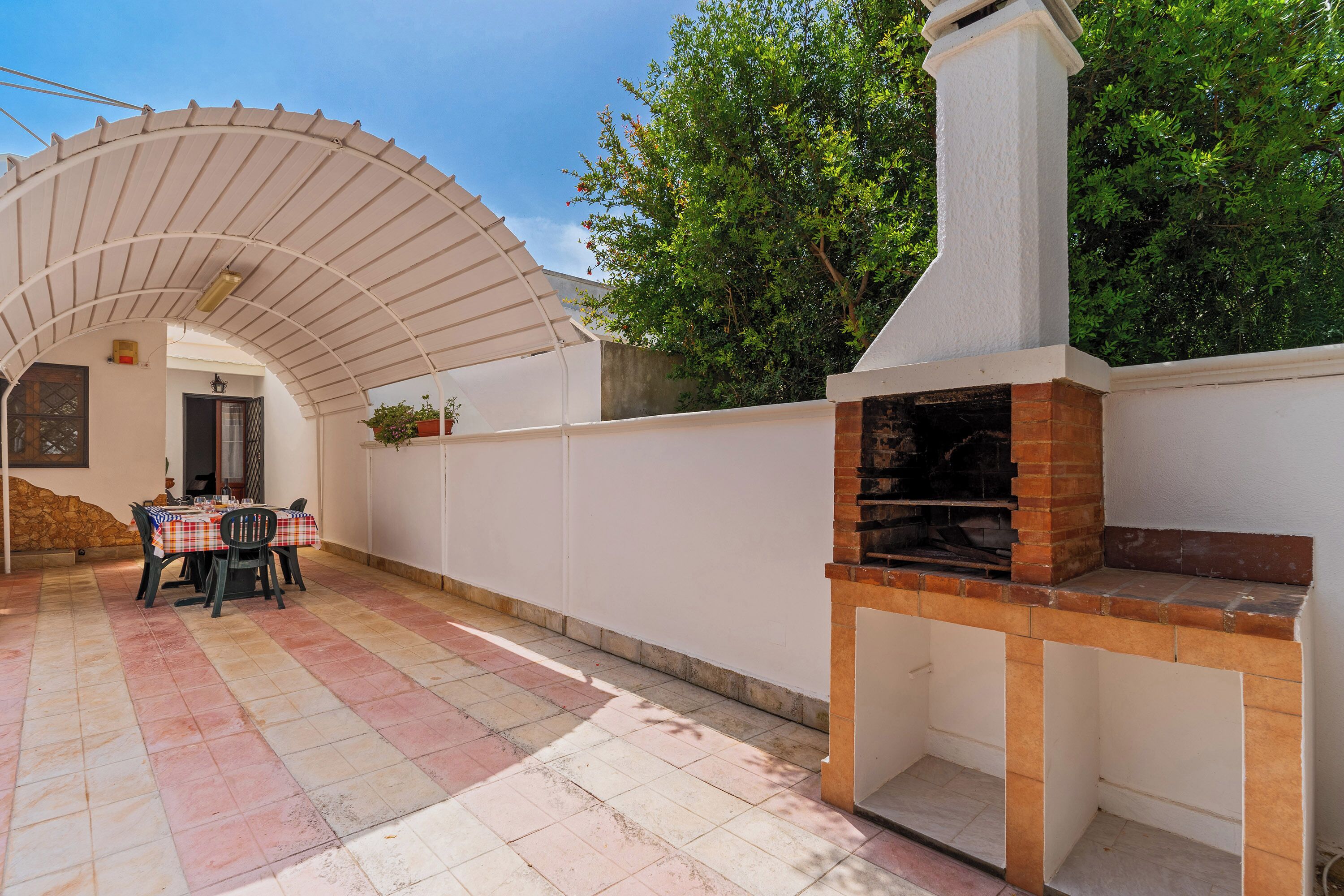 Une terrasse extérieure avec une table et des chaises, un four en briques et un mur blanc avec une fenêtre.