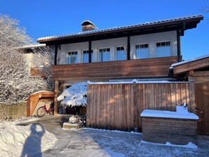 Een huis met twee verdiepingen, een houten terras, een overdekte veranda en een hek vol sneeuw.