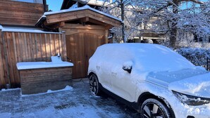 Ein mit Schnee bedecktes Auto vor einem Holzhaus mit einem Pflasterweg.
