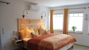 Ein Schlafzimmer mit einem hölzernen Kopfteil, einem Bett mit brauner Decke, zwei Nachttischlampen, einem Nachttisch und einem Fenster mit Vorhängen.