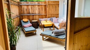 Un espace extérieur accueillant, aménagé avec du mobilier en bois, notamment une table et des bancs, et offrant une vue sur un jardin.