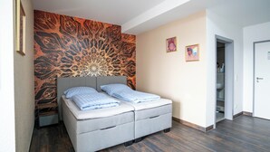 A bedroom with a grey bed, a patterned wall, and a door leading to a bathroom. - Apartment with shower (Garbsen)