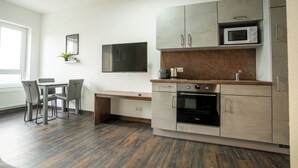 A modern kitchen with grey cabinets, a microwave, an oven, and a dining area with a table and chairs. - Apartment with shower (Garbsen)