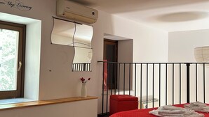 Quarto com cama vermelha, janela com vista, parede branca com frase decorativa e um banco vermelho.
