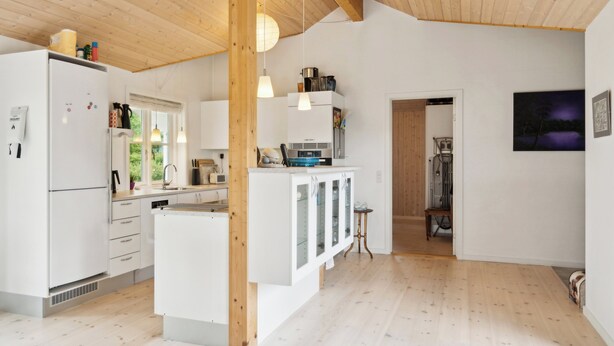 Una cucina moderna con mobili bianchi, un'isola centrale, illuminazione a sospensione e vista all'esterno.