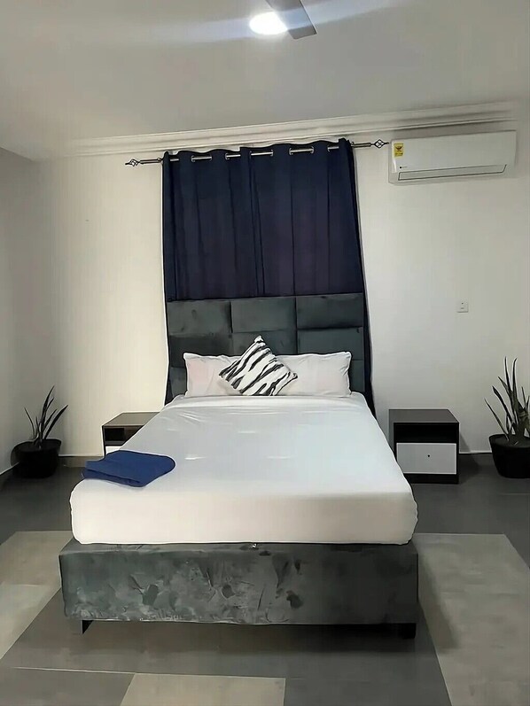 A modern bedroom with a large bed, dark curtains, and a ceiling fan.