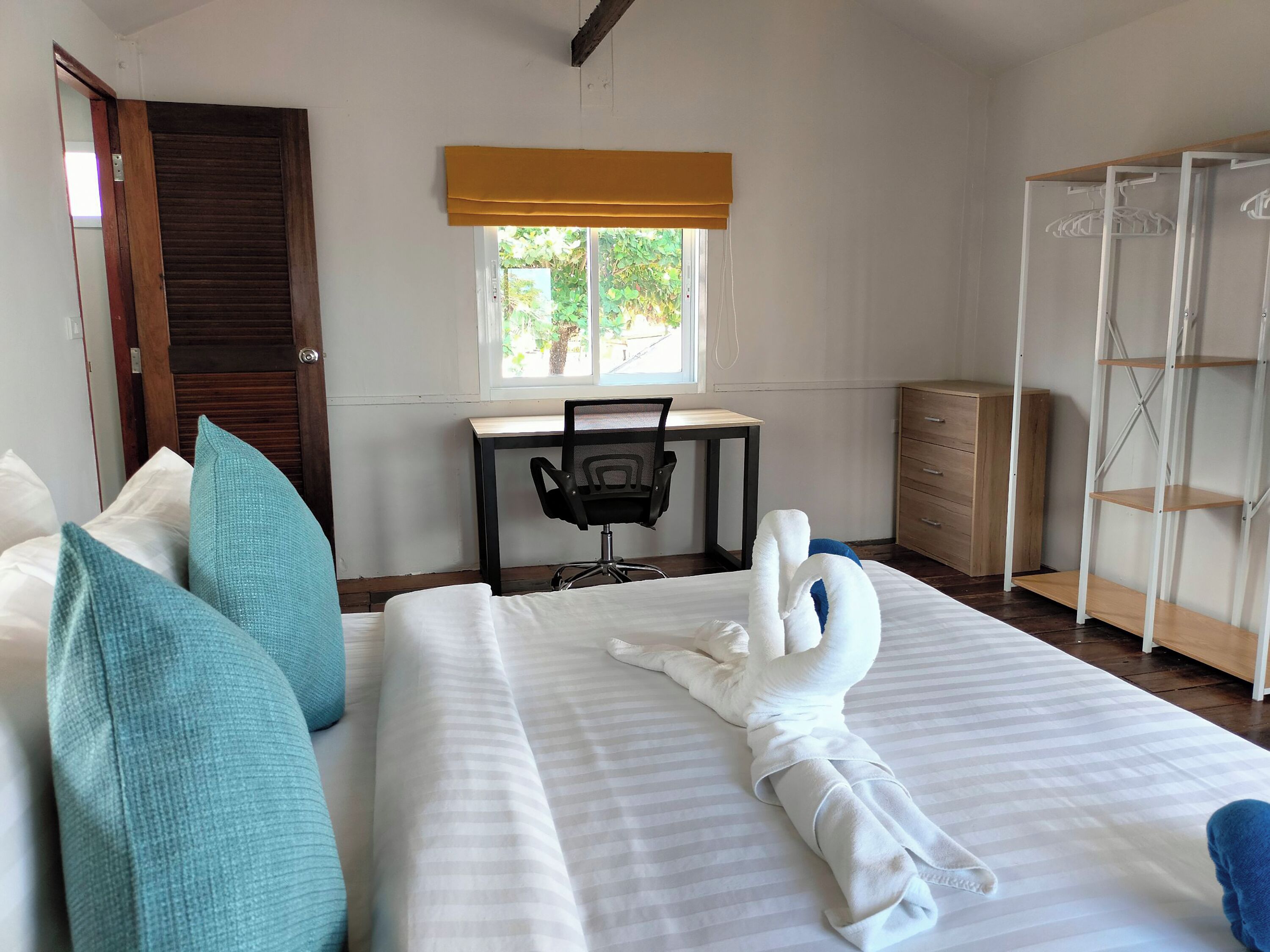 A hotel room with a bed, a desk, a chair, a wardrobe, and a window with a view of greenery.