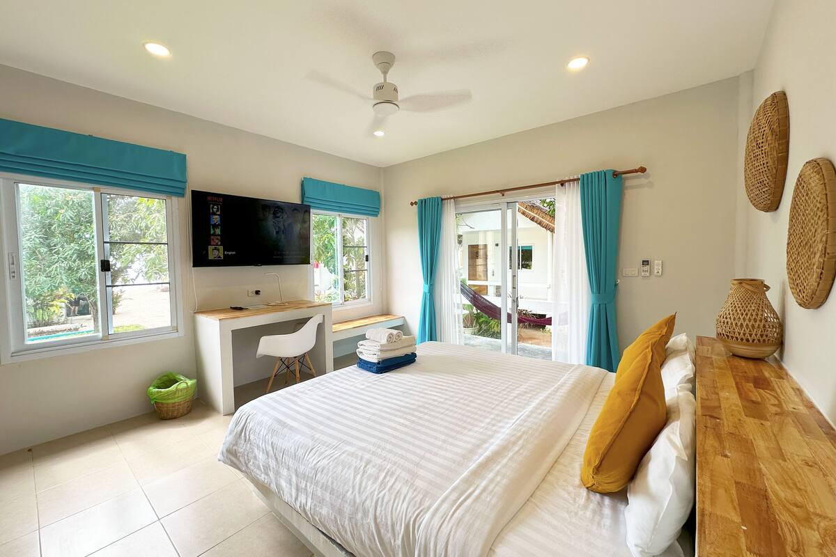 A bedroom with a bed, a desk, a chair, a TV, and a window.
