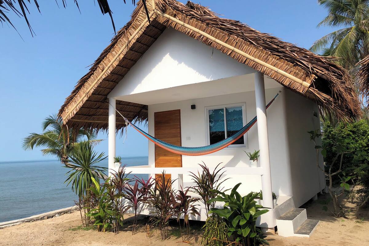A beach house with a thatched roof, a hammock, and a view of the ocean.