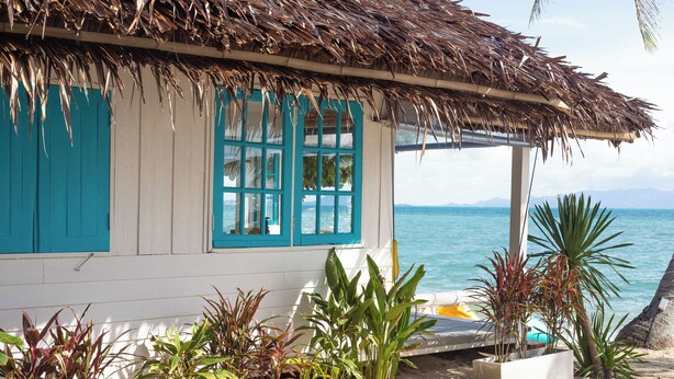 A beach house with a thatched roof, turquoise shutters, and a view of the ocean. - Sand Terrace Beach Bungalows (Ko Pha-ngan)