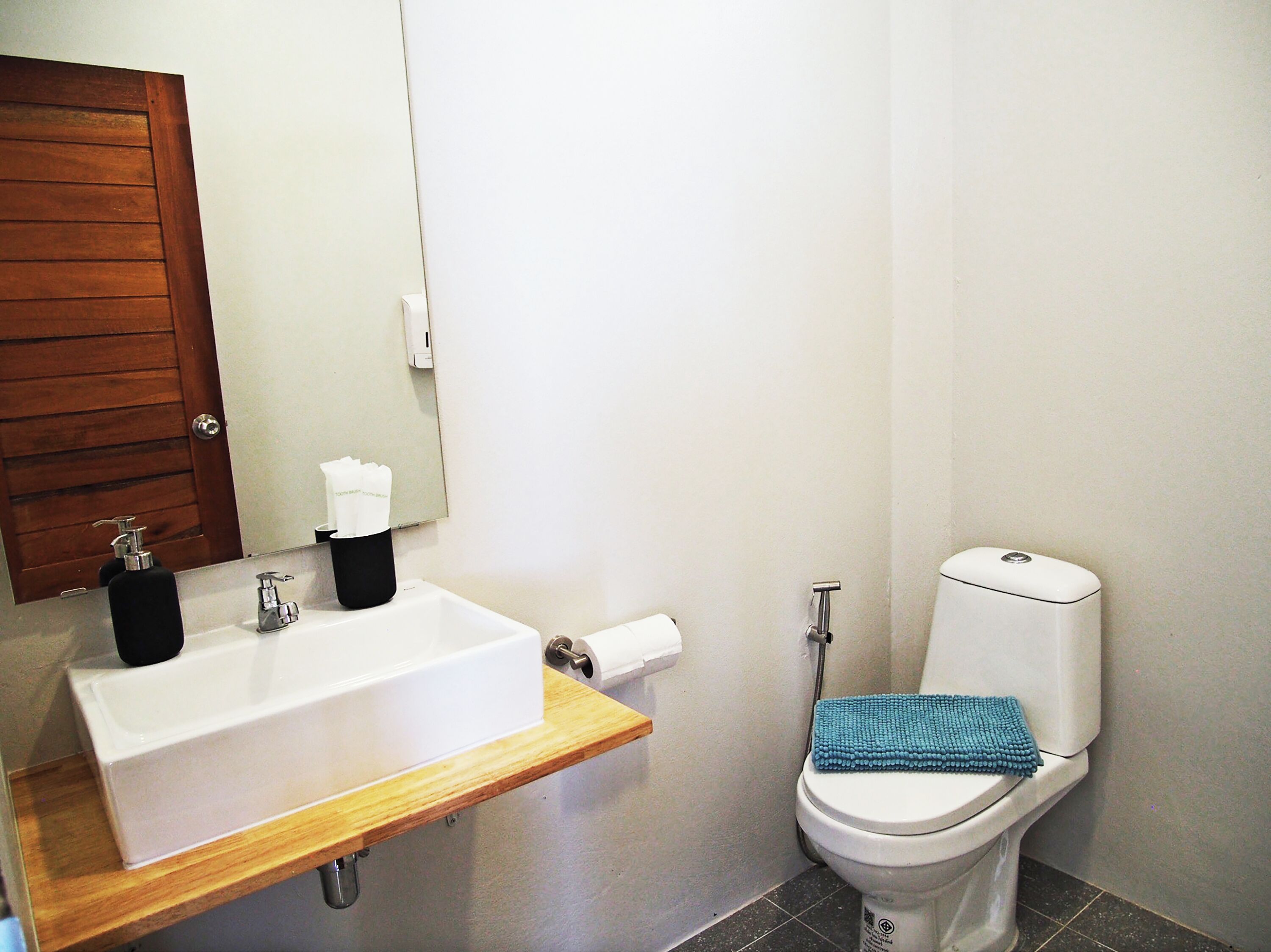 Un bagno con un lavandino bianco, uno specchio, un water e una mensola in legno.