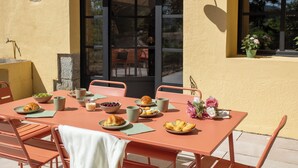 Ein Essbereich im Freien mit einem Tisch, der für ein Frühstück gedeckt ist, darunter Croissants, Obst und Kaffee.