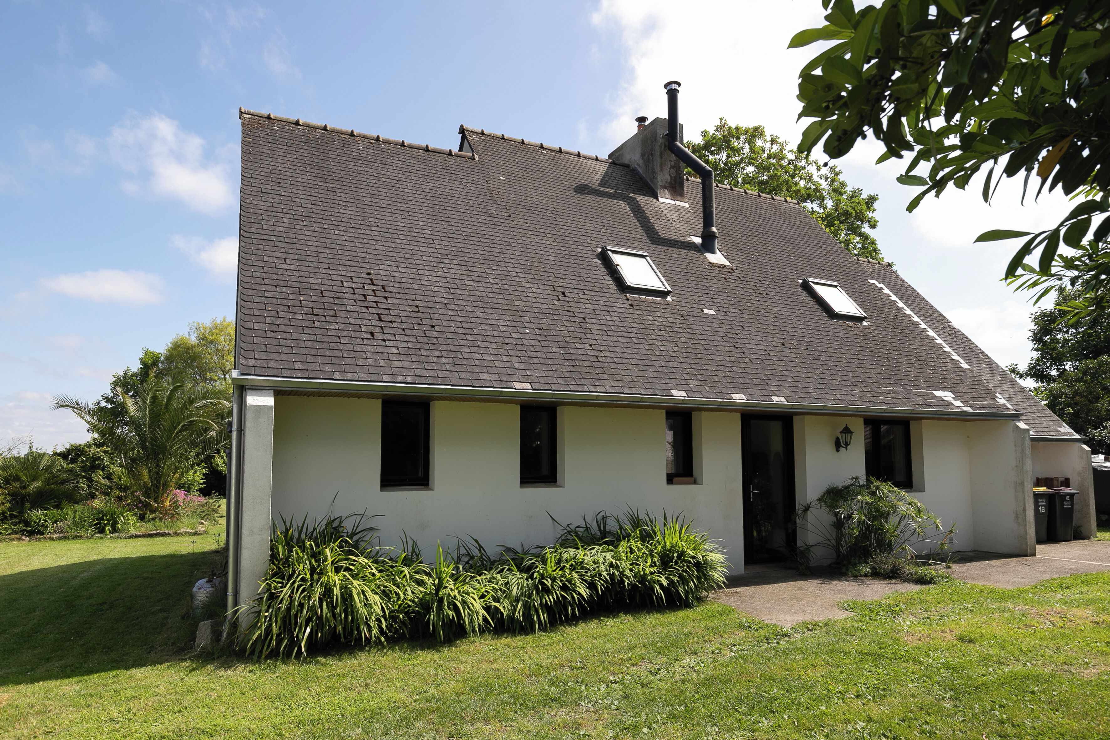 Une maison de plain-pied avec un toit en pente, une cheminée et un petit garage attenant.