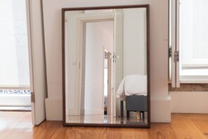 Un mirall reflecteix un espai amb sòl de fusta, una porta blanca i una cadira grisa.