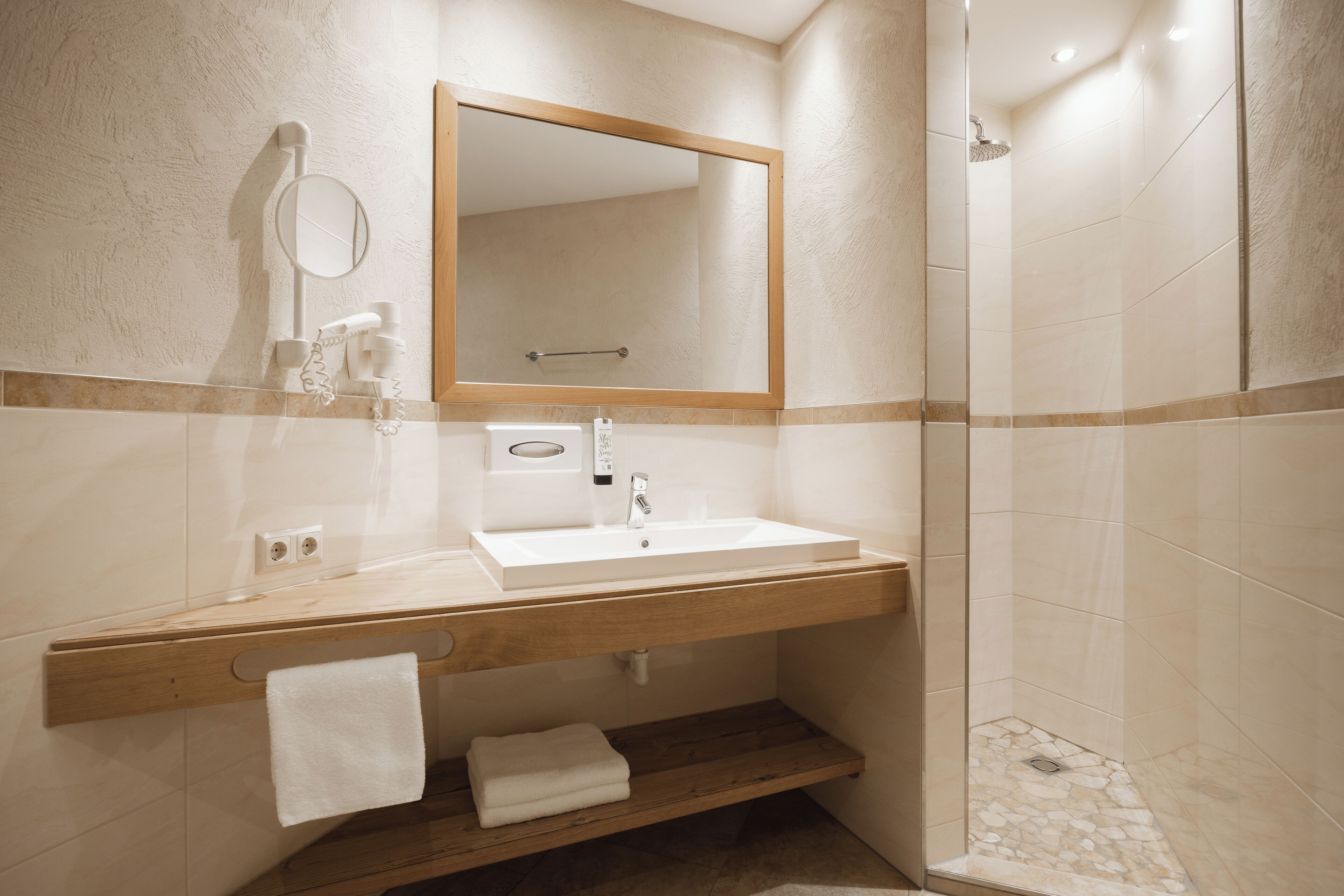 A bathroom with a wooden vanity, a sink, a mirror, a towel rack, and a shower area.