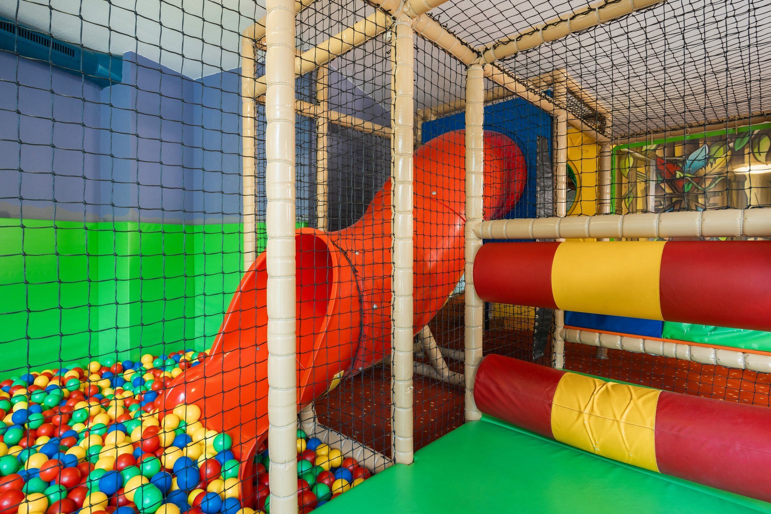 Area giochi al chiuso con scivolo, piscina di palline e strutture imbottite.
