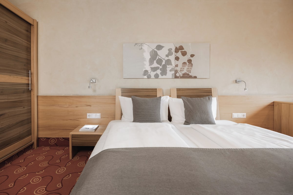 Ein Hotelzimmer mit einem Bett, einem Nachttisch, einem hölzernen Kopfteil, einem Wandbild und einem roten Teppich mit Muster.