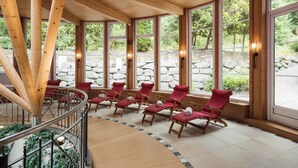 A wooden interior with large windows, stone walls, and red cushioned chairs. - miaflor Familien- & Aktivresort (Ried im Oberinntal)