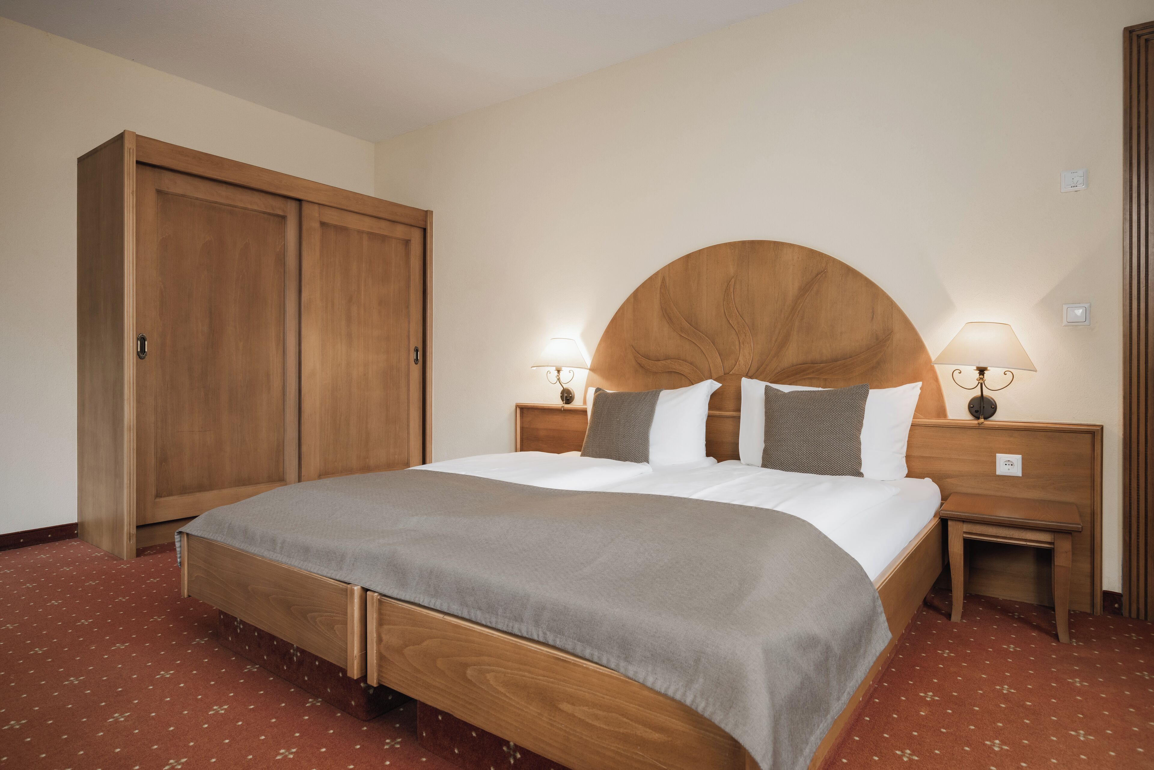 Ein Hotelzimmer mit einem großen Bett, einem Holzkopfteil, zwei Nachttischen mit Lampen und einem Kleiderschrank.