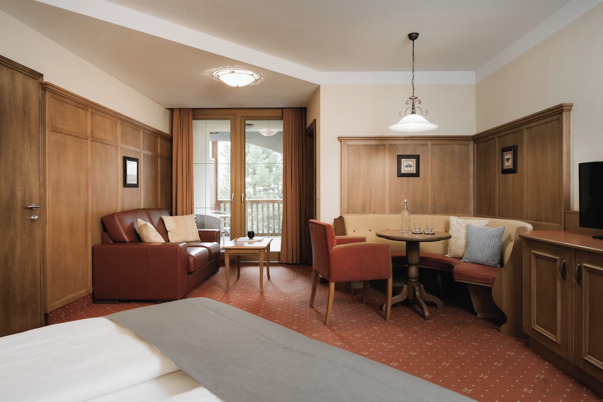 Ein Hotelzimmer mit Bett, Sofa, Esstisch mit Stühlen, Fernseher und Holzschränken.