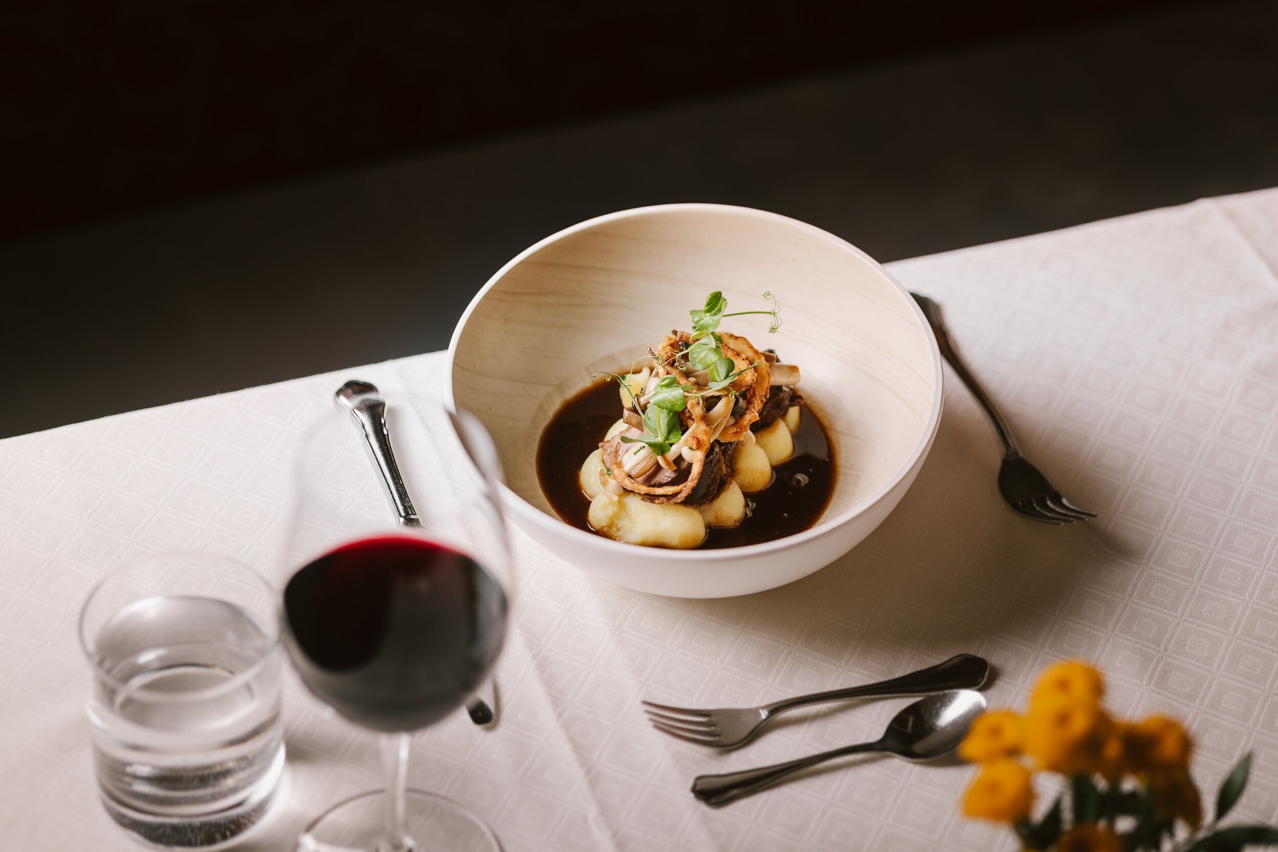 A dining table with a bowl of food, a wine glass, and cutlery.