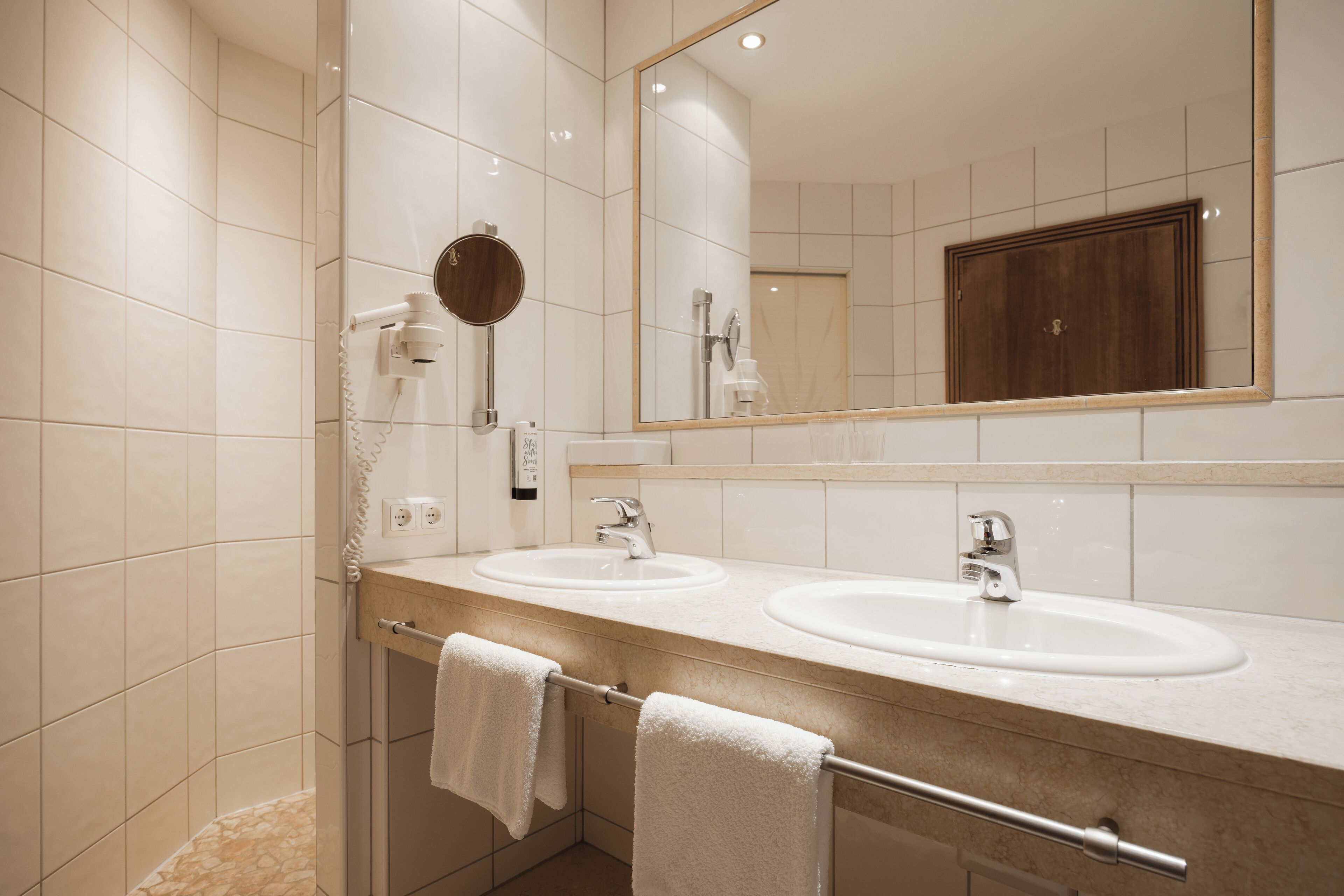 A modern bathroom with two sinks, a large mirror, and a towel rack.