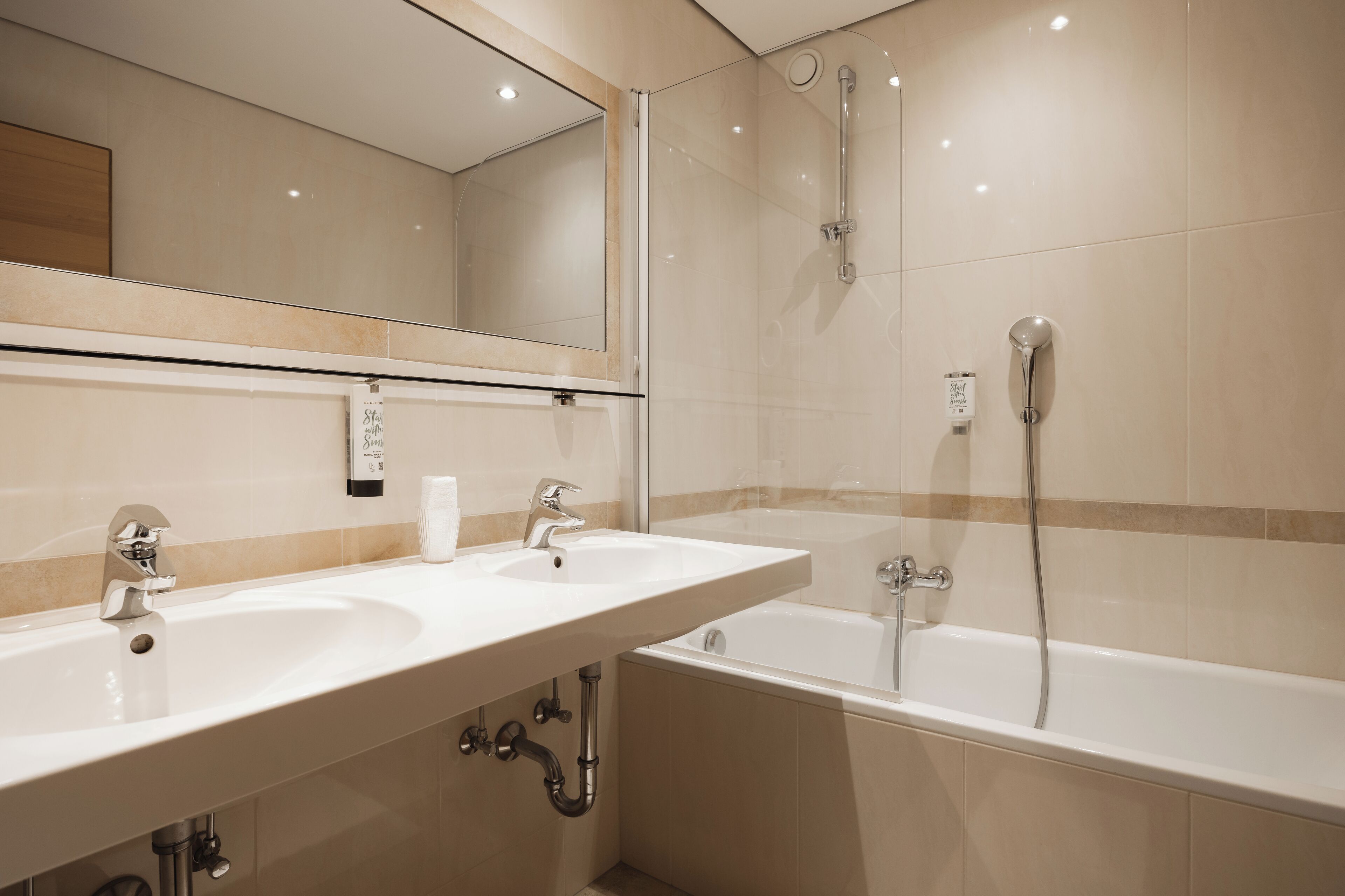 Een moderne badkamer met twee wastafels, een bad en een douche met glazen wanden.