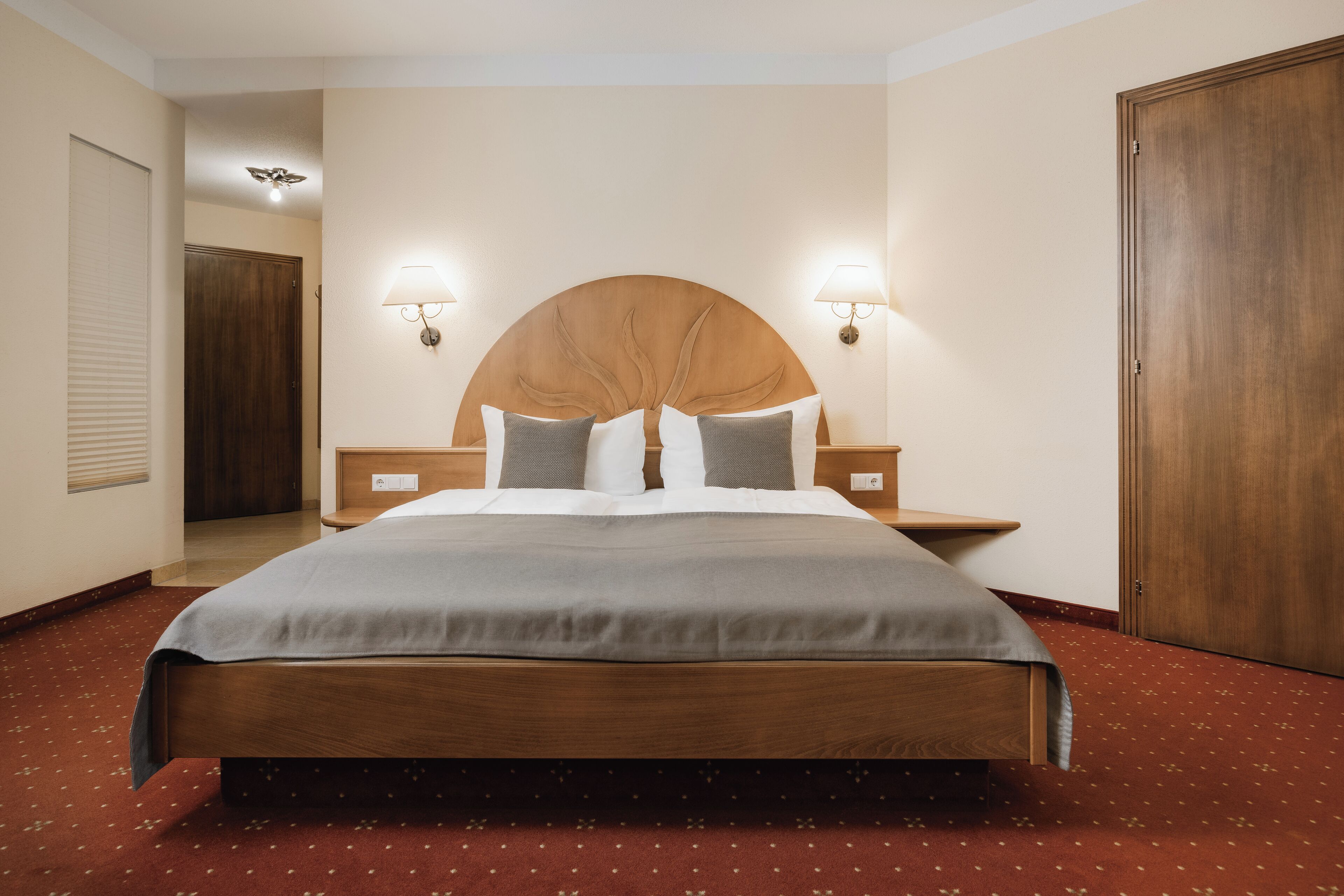Una camera d'albergo con un letto grande, una testiera in legno, due comodini e un pavimento coperto da tappeto rosso.