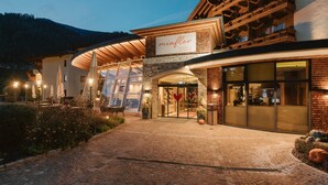 A hotel with a modern design, featuring a prominent entrance, a covered outdoor area, and a mountain backdrop. - miaflor Familien- & Aktivresort (Ried im Oberinntal)