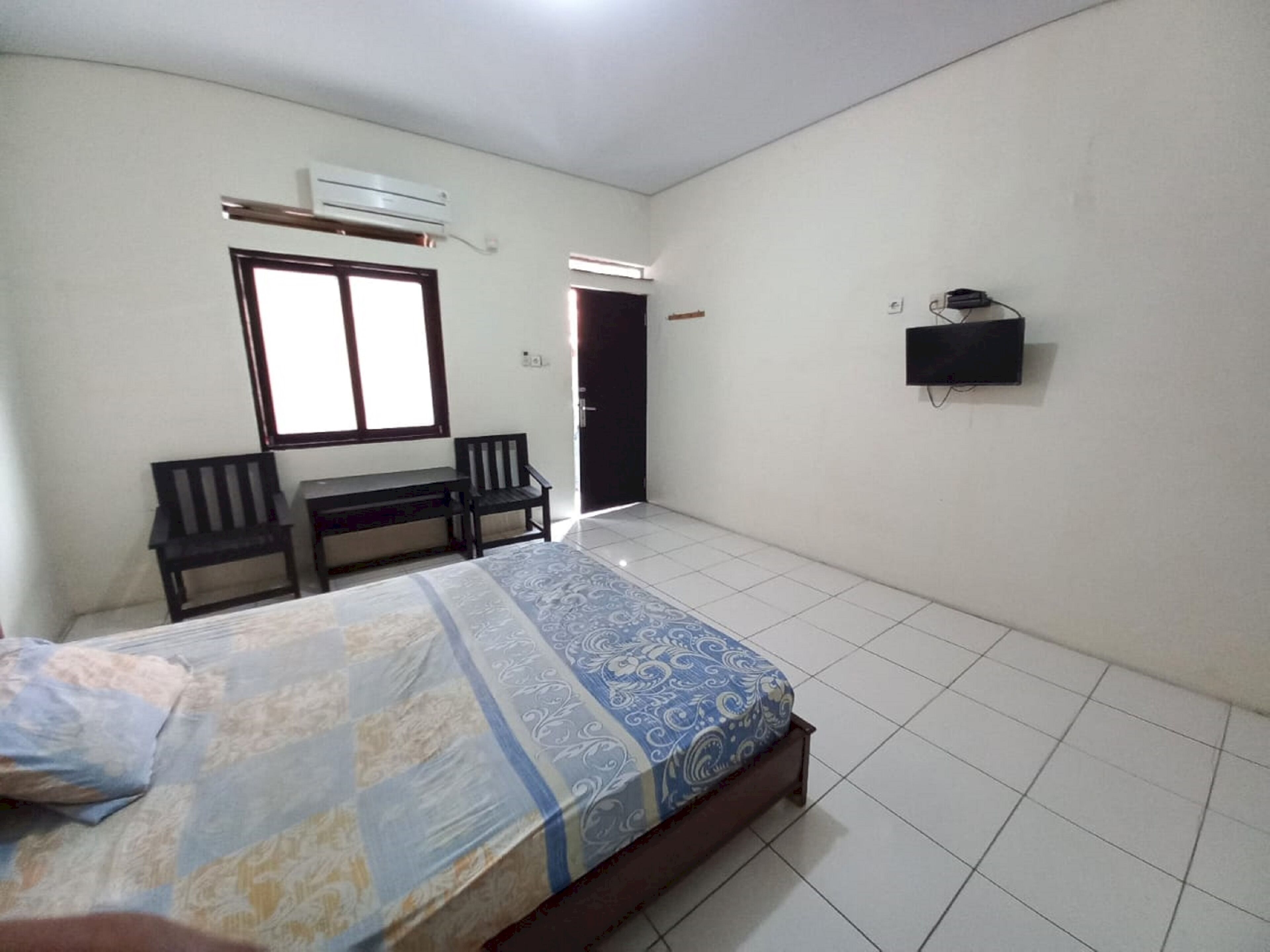 Un dormitorio con una cama, dos sillas, un escritorio, aire acondicionado, televisor y una puerta.
