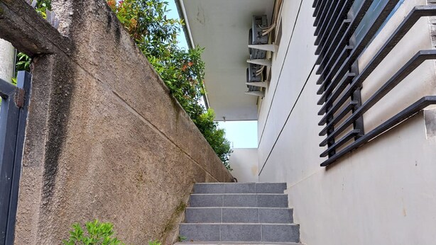 Una escalera que sube hacia un edificio, con un muro de concreto a un lado y una barandilla de metal al otro.