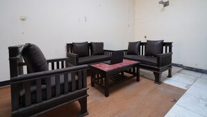 Una sala de estar con muebles de madera oscura, incluyendo un sofá y sillones, una mesa de centro y una pequeña mesa con una computadora portátil.