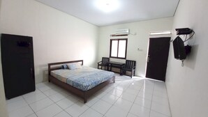 Un dormitorio con cama, escritorio y silla. Hay una ventana, aire acondicionado y una puerta.