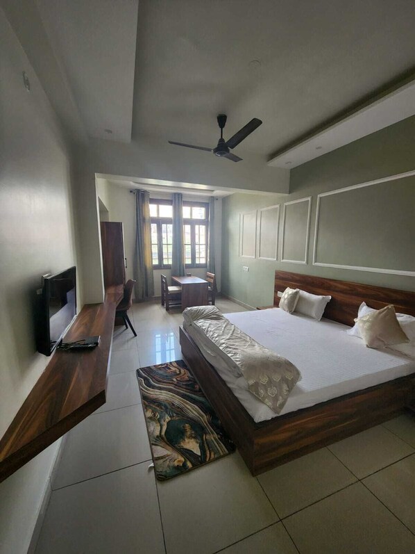Une chambre d’hôtel avec un grand lit, un bureau avec une chaise, une télévision et un ventilateur de plafond.