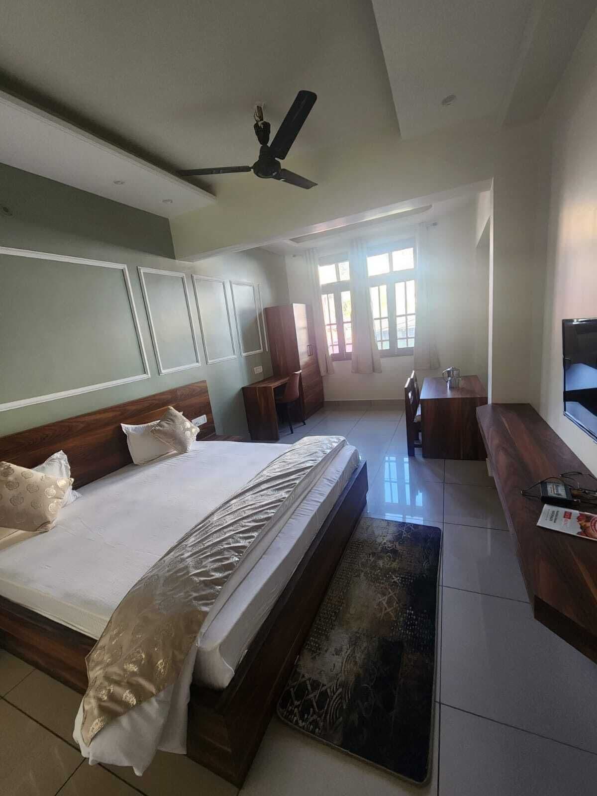 A bedroom with a large bed, a desk, a chair, a TV, and a ceiling fan.