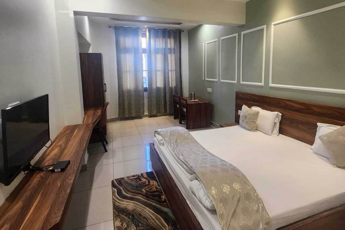 A hotel room with a bed, a TV, a desk, a chair, a ceiling fan, and a window with curtains.