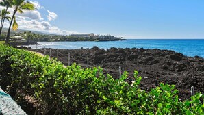 A coastal landscape with a rocky shoreline, a clear blue sky, and a distant view of a resort area.