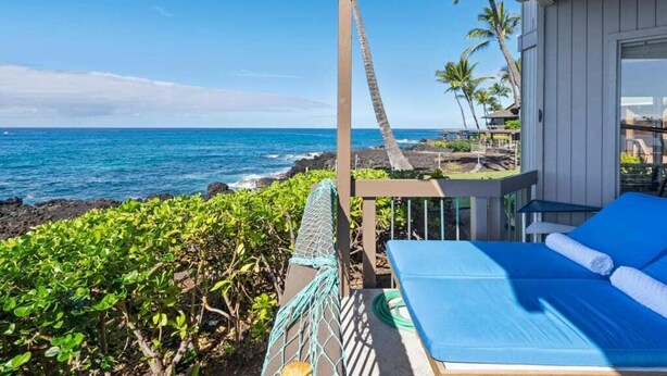 A beachside room with a view of the ocean, a hammock, and a bed with blue bedding.