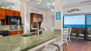 A kitchen with a large island, bar stools, and a view of the ocean.