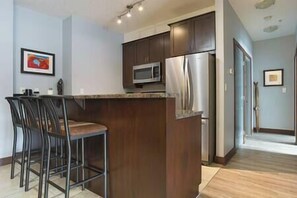 A kitchen with dark wooden cabinets, a stainless steel refrigerator, a microwave, and a bar area with stools.