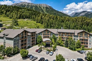 A multi-story hotel with a parking lot, surrounded by forested hills and mountains. - Mtn Views + Bunk Room / Pool, Hot Tub, Sleeps 6 (Fernie)