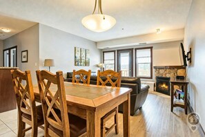 A dining area with a wooden table and chairs, a fireplace, and a view of the outdoors through large windows. - Mtn Views + Bunk Room / Pool, Hot Tub, Sleeps 6 (Fernie)