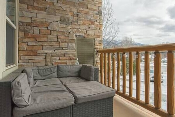 A balcony with a stone wall, a grey sofa, and a wooden railing.
