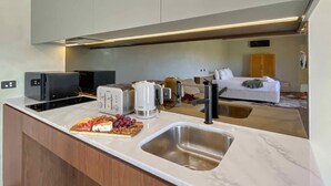 Eine moderne Küche mit integrierter Kochinsel, Spüle und Essbereich mit Sofa und Bett im Hintergrund.